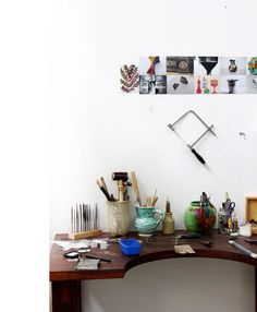 a wooden desk topped with lots of clutter next to a wall mounted art piece