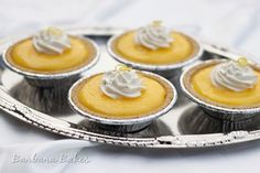 small cupcakes with whipped cream on top are sitting in silver tins, ready to be eaten