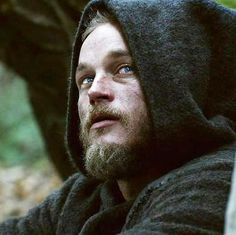 a man with a beard and blue eyes wearing a black hoodie looking off into the distance