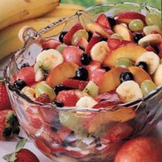 a glass bowl filled with fruit on top of a table next to bananas and strawberries