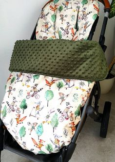 a baby stroller seat cover with trees and animals on it's side, sitting next to a potted plant