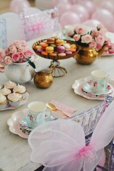 a table topped with plates and cups filled with cupcakes next to pink balloons