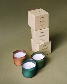 three candles sitting next to each other in front of boxes on a table with one candle lit