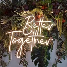 a neon sign that says better together surrounded by greenery