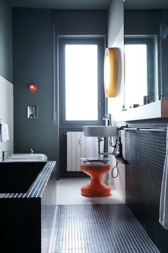 a modern bathroom with black and white tiles on the floor, orange pedestal sink, and large window