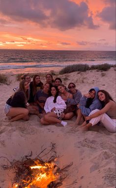 a group of women sitting around a campfire on the beach at sunset or sunrise