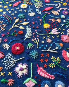 a close up of a blue cloth with various colored stitches and flowers on it,