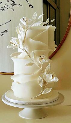 a white wedding cake sitting on top of a table in front of a round mirror