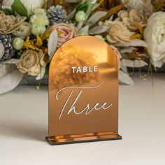 a table sign that says table these with flowers in the back ground and behind it