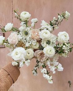 a person holding a bouquet of flowers in front of a pink wall with white flowers