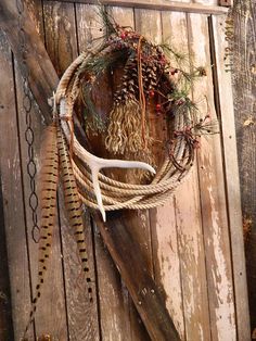 a rustic wreath with antlers and pine cones hanging on a wooden door, decorated with rope