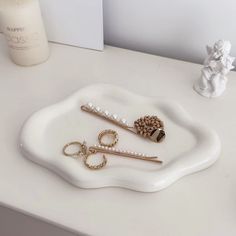 a white tray topped with three different types of hair pins and pearls on top of a table