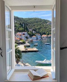 an open book sitting on top of a window sill next to a body of water