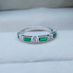 a diamond and emerald ring sitting on top of a white cloth