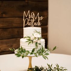 a white wedding cake with greenery and a wooden mr and mrs sign on top