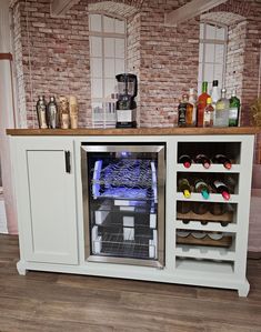 a white cabinet with wine bottles and glasses on the top, in front of a brick wall