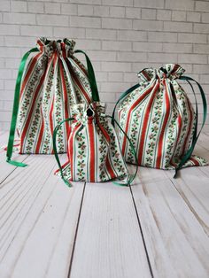 two bags with green and red ribbons on them sitting on a white wooden floor next to a brick wall