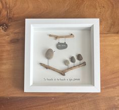 a white frame with rocks and birds in it on a wooden table next to a piece of driftwood