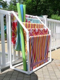 two towels are hanging from a white rack on the side of a fence, next to a pool