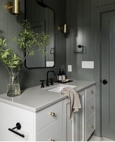 a bathroom with gray walls and white countertops, gold fixtures and a plant in a vase on the sink