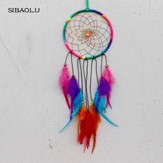 a multicolored dream catcher hanging on a white wall with feathers attached to it