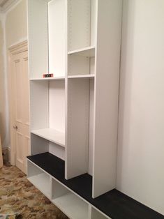 an empty room with white cabinets and black shelves on the floor in front of a carpeted wall