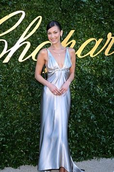 a woman standing in front of a green wall wearing a silver dress and black heels