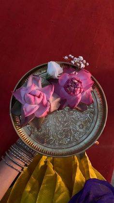 pink flowers are placed on a silver plate next to yellow and purple cloth, with other items in the background