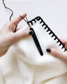 a woman is holding a black and white piece of cloth while knitting it with scissors