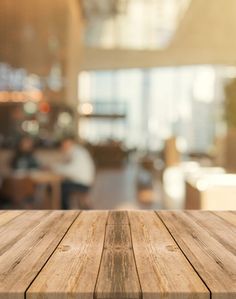 an empty wooden table top in front of a blurry room with people sitting at tables