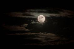 the full moon is shining brightly in the night sky with clouds and dark blue skies