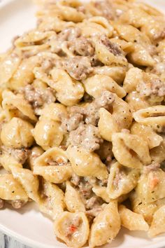 a white plate topped with macaroni and cheese covered in ground beef sauce on top of a wooden table