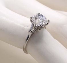 a diamond ring sitting on top of a white gloved hand with the band down