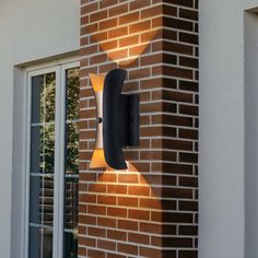 a modern outdoor wall light on the side of a brick building with an open window