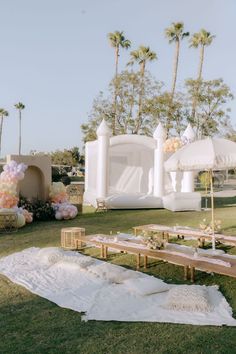 an outdoor wedding setup with tables, umbrellas and flowers on the grass in front of palm trees