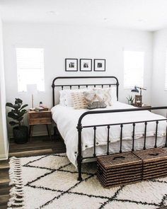 a bedroom with white walls and black iron bed frame, rugs on the floor