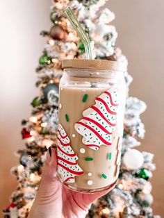 a hand holding up a mason jar decorated with candy canes and christmas decorations next to a tree