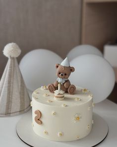 a small teddy bear sitting on top of a white cake