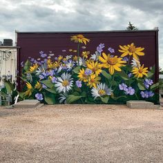 a mural painted on the side of a building with yellow and white flowers in front