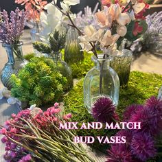 various vases filled with flowers on top of a table covered in moss and dirt