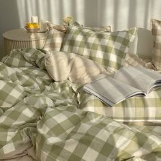 an open book sitting on top of a bed covered in green and white checkered sheets