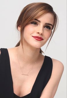 a woman wearing a black dress with a gold necklace on her neck and red lips