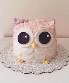 an owl cake with pink frosting and black eyes on a doily platter