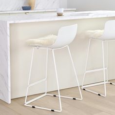 two white bar stools sitting in front of a counter with a marble slab top