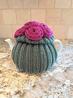 a crocheted tea pot with a flower on top sits on a marble counter