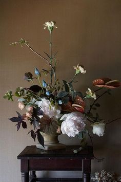 a vase filled with lots of flowers on top of a wooden table next to a wall