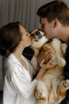 a man and woman kissing while holding a small dog in their arms, both wearing white