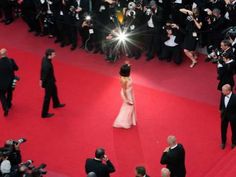 a woman in a pink dress is walking down the red carpet with cameras around her