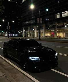 a black sports car is parked on the side of the road at night in front of an office building