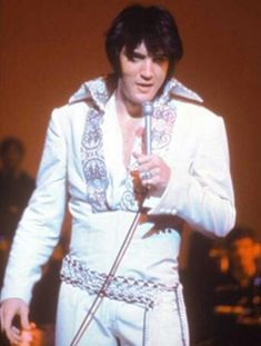 elvis presley singing into a microphone while wearing white suit and holding a microphone in his right hand